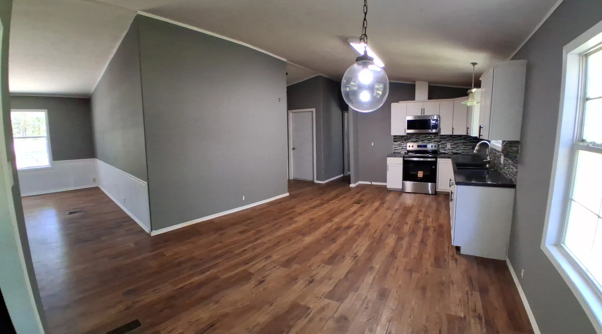 Open-concept layout with wood-finish flooring, a kitchen with white cabinetry, stainless steel appliances, and a custom-finish countertop