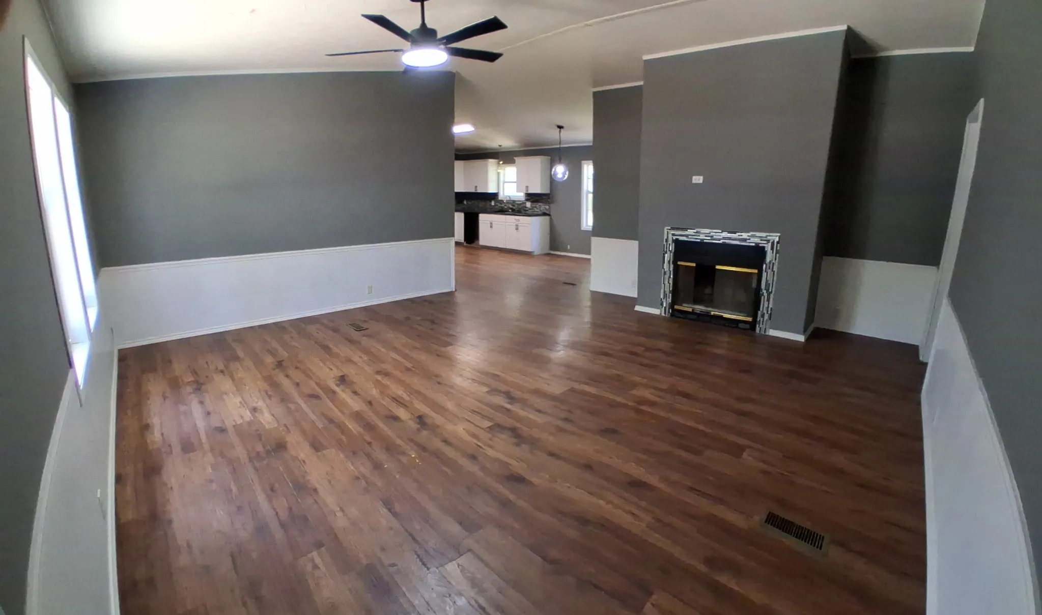 Spacious living area featuring wood-finish flooring, a ceiling fan, and a fireplace with a decorative tile surround