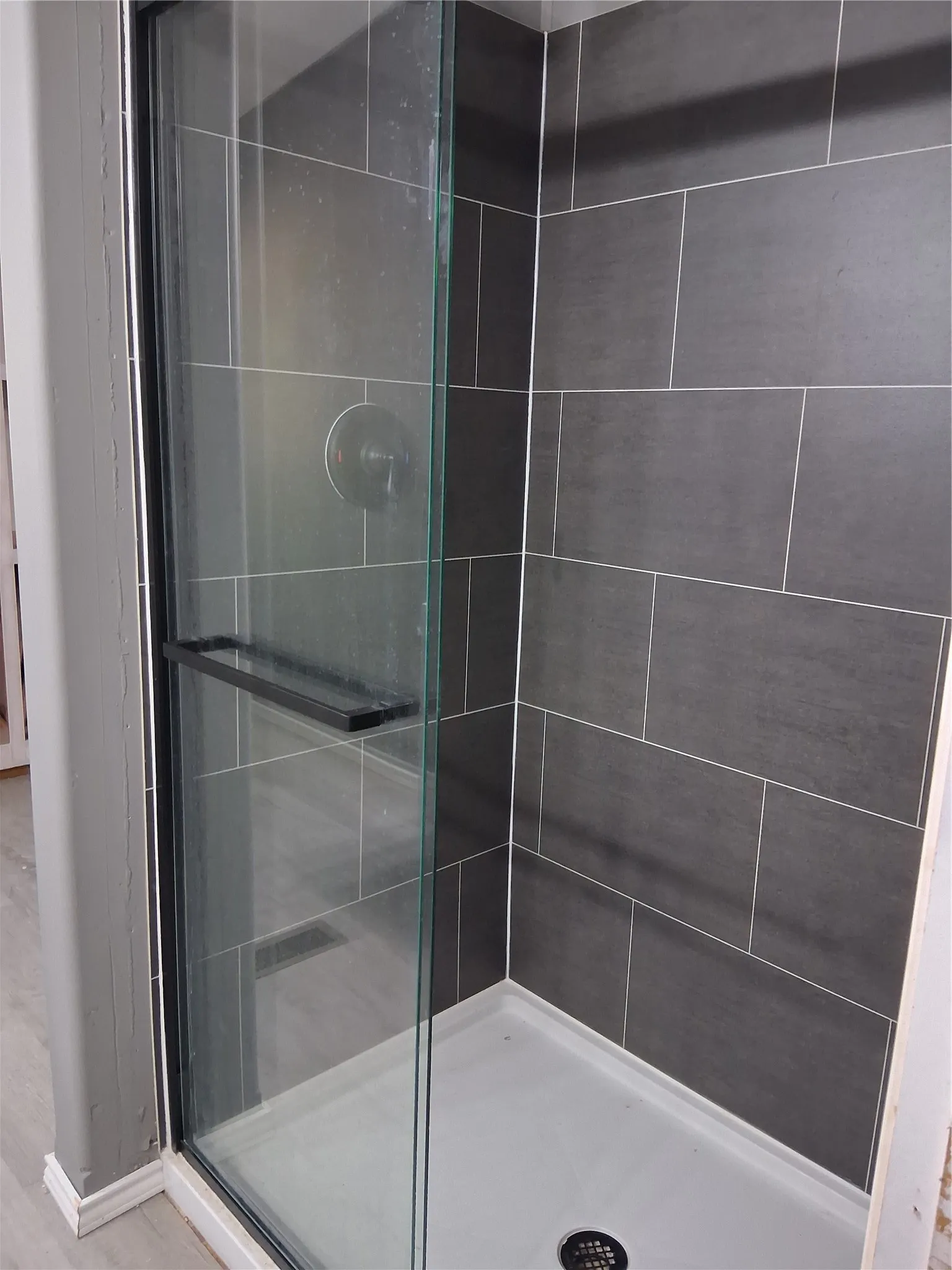 Frameless glass shower enclosure featuring dark rectangular wall tiles, a white shower pan, and a single-handle shower valve