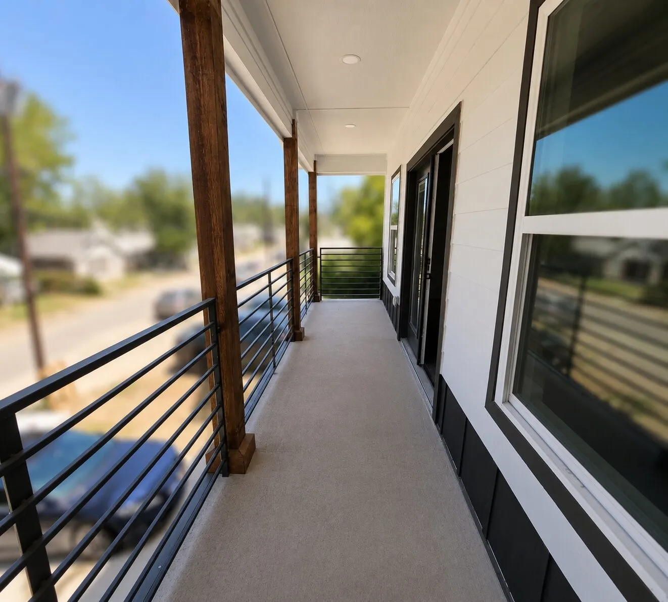 Covered concrete balcony with exposed wood columns, black horizontal metal railings, and recessed lighting
