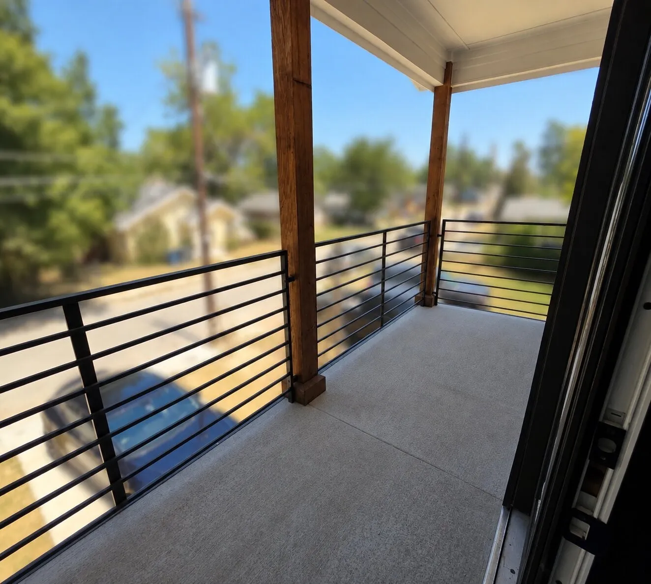 Balcony with exposed wood structural beams, concrete flooring, and horizontal metal railings