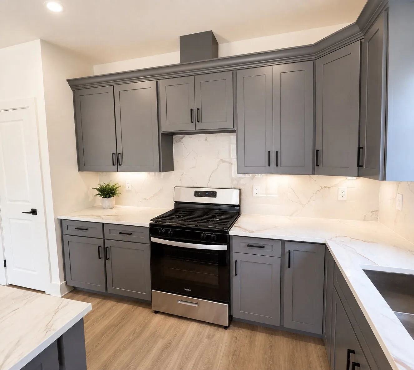 Gray shaker-style cabinetry with crown molding, stainless steel range, white countertops with veining, and wood-finish flooring