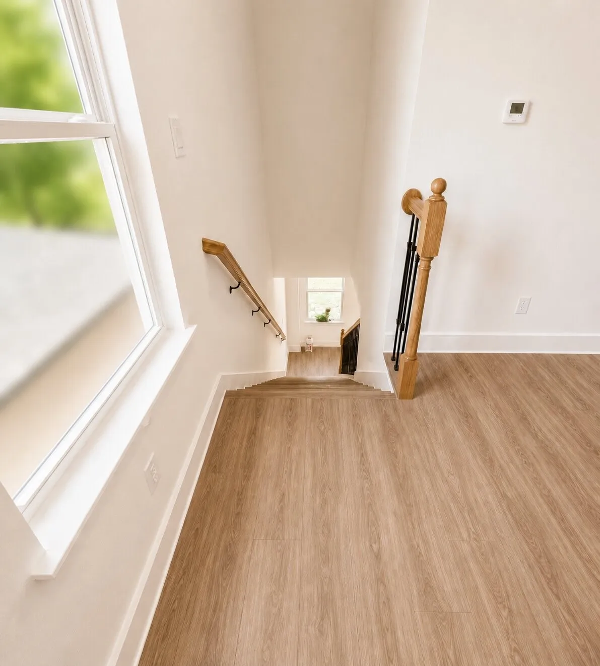 Wood-finish flooring throughout, bright white walls, white window trim, and a natural wood handrail with black balusters