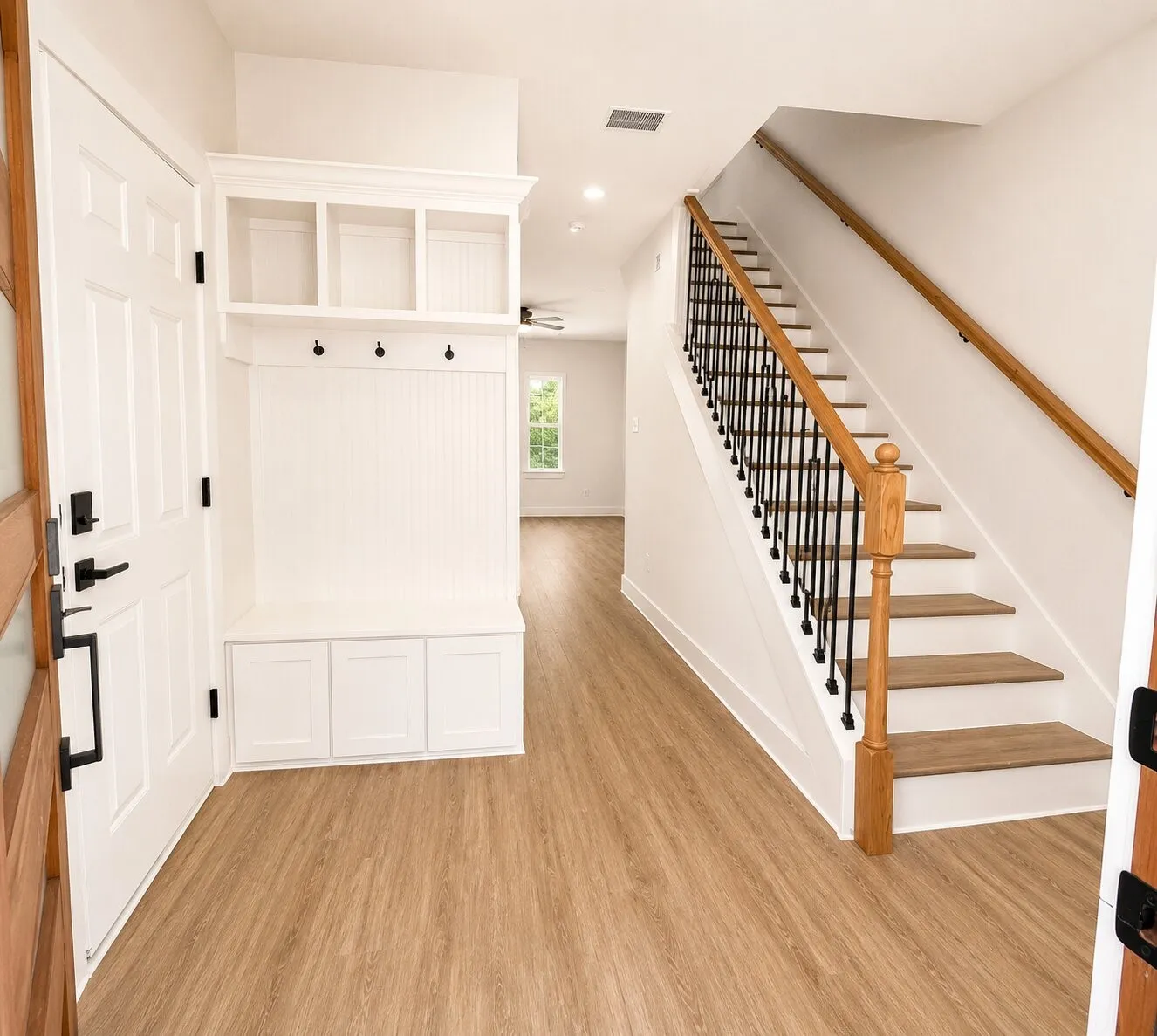 Entryway with wood-finish flooring, built-in mudroom storage, and staircase featuring wood handrails and black metal balusters