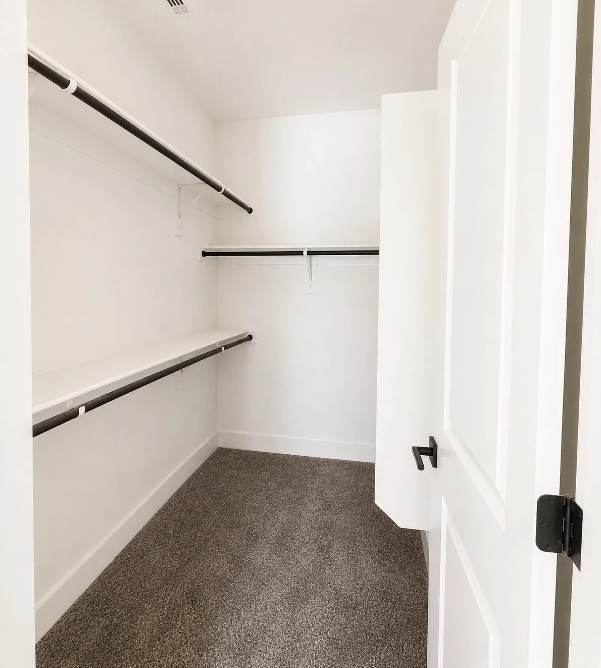 Walk-in closet with white walls, three rows of shelving, black clothing rods, and gray carpet flooring