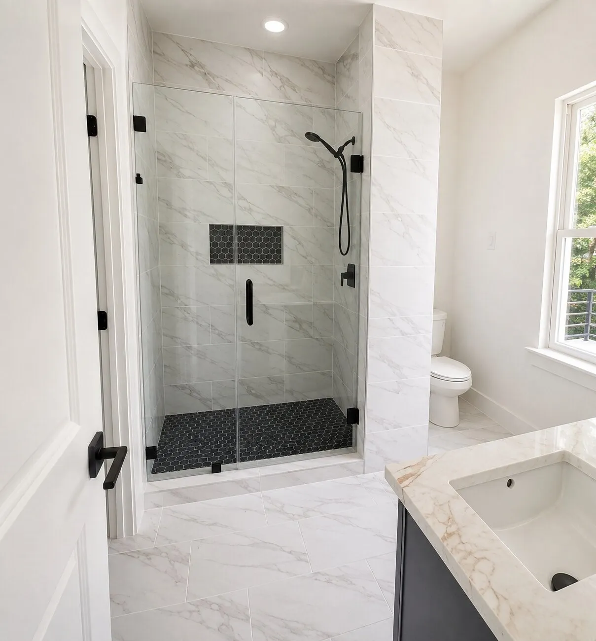 Glass-enclosed shower with black hexagon tile flooring and a recessed shelf