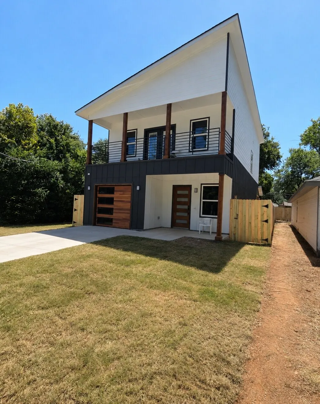 Contemporary two-story exterior with a striking roofline, featuring a wood-finish garage door, a second-story balcony with metal railings, and a concrete driveway
