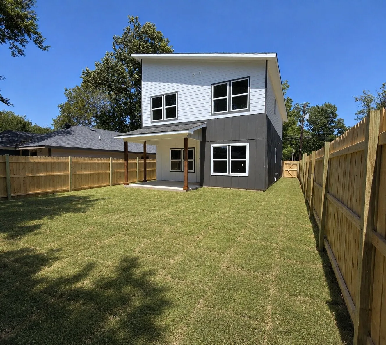 Expansive backyard featuring a manicured lawn, full privacy fencing, and a covered patio with wooden posts