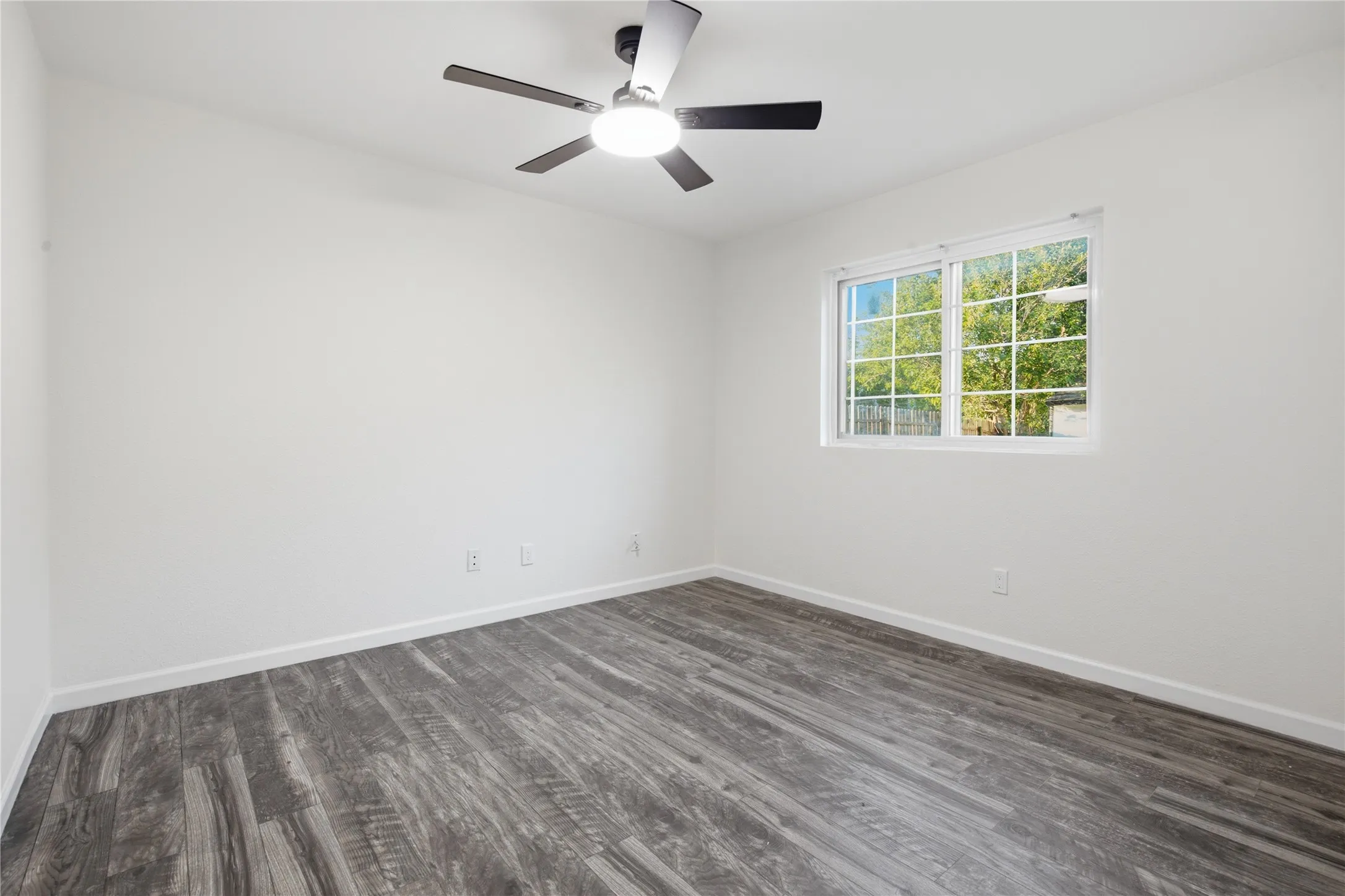 Wood-finish flooring, white walls, ceiling fan with integrated lighting, and a single window with white trim