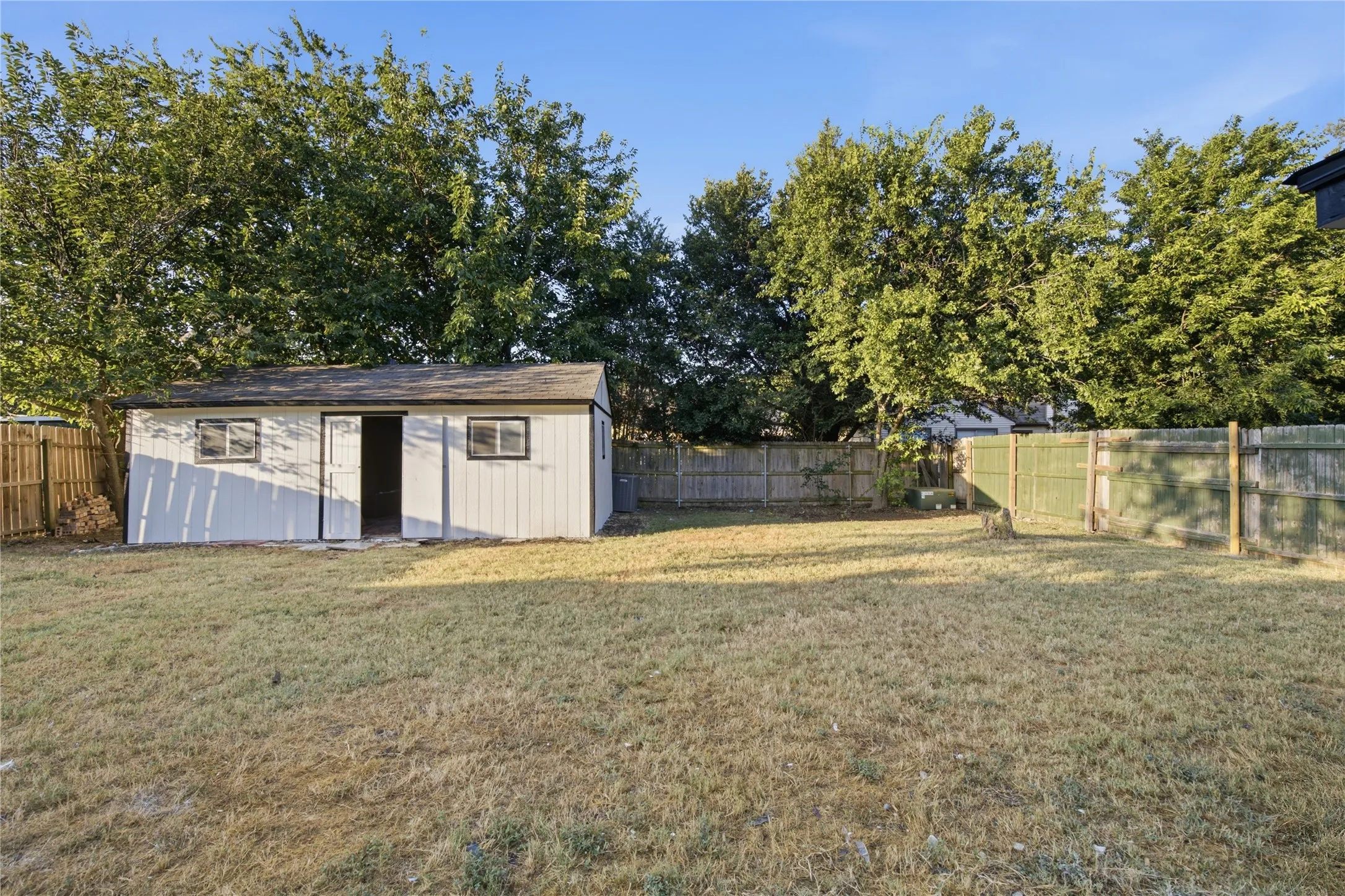 Expansive outdoor space featuring a detached storage shed, mature trees, and a perimeter fence