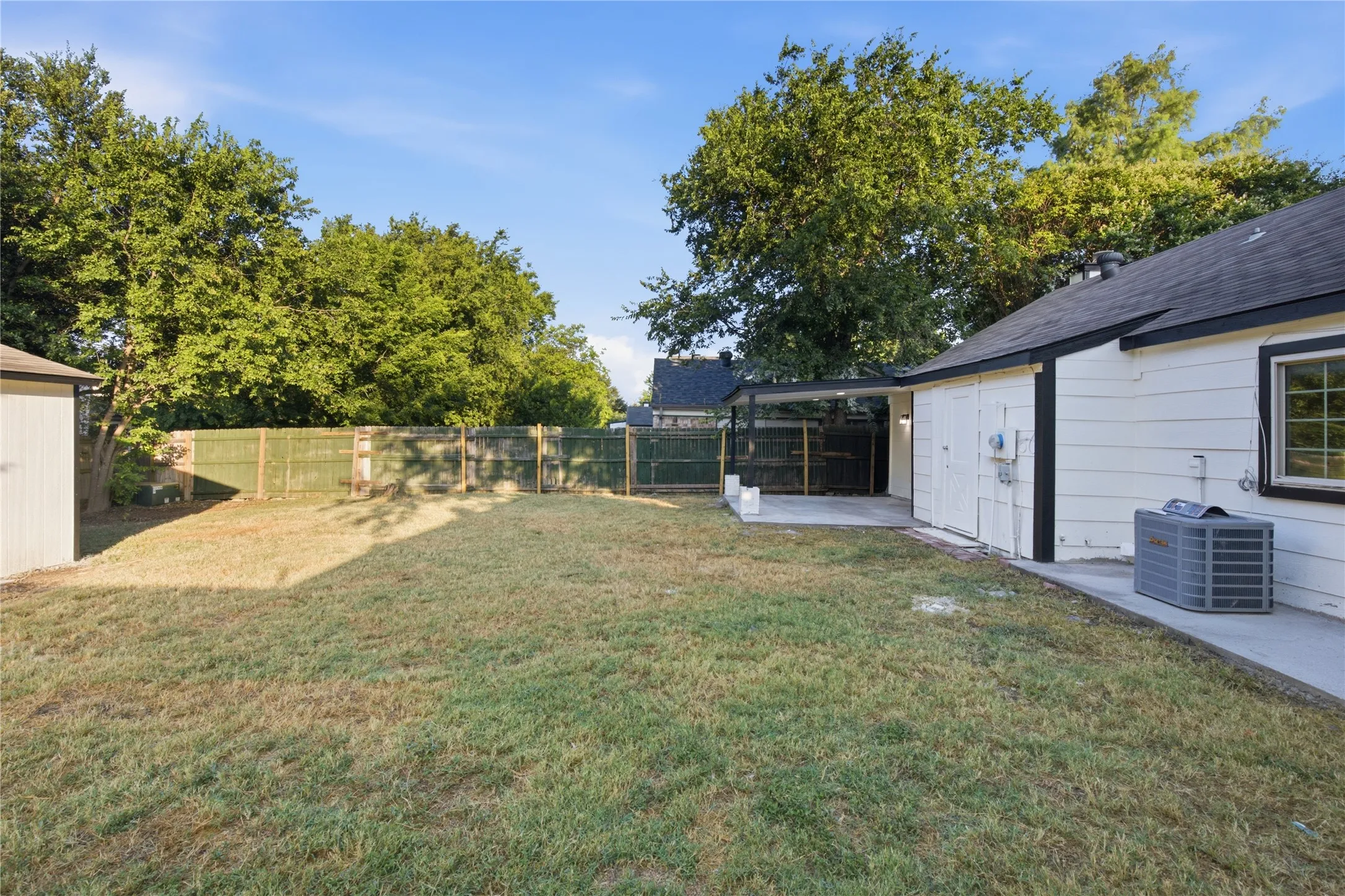 Expansive lawn area with a solid panel fence, concrete patio, and mature trees