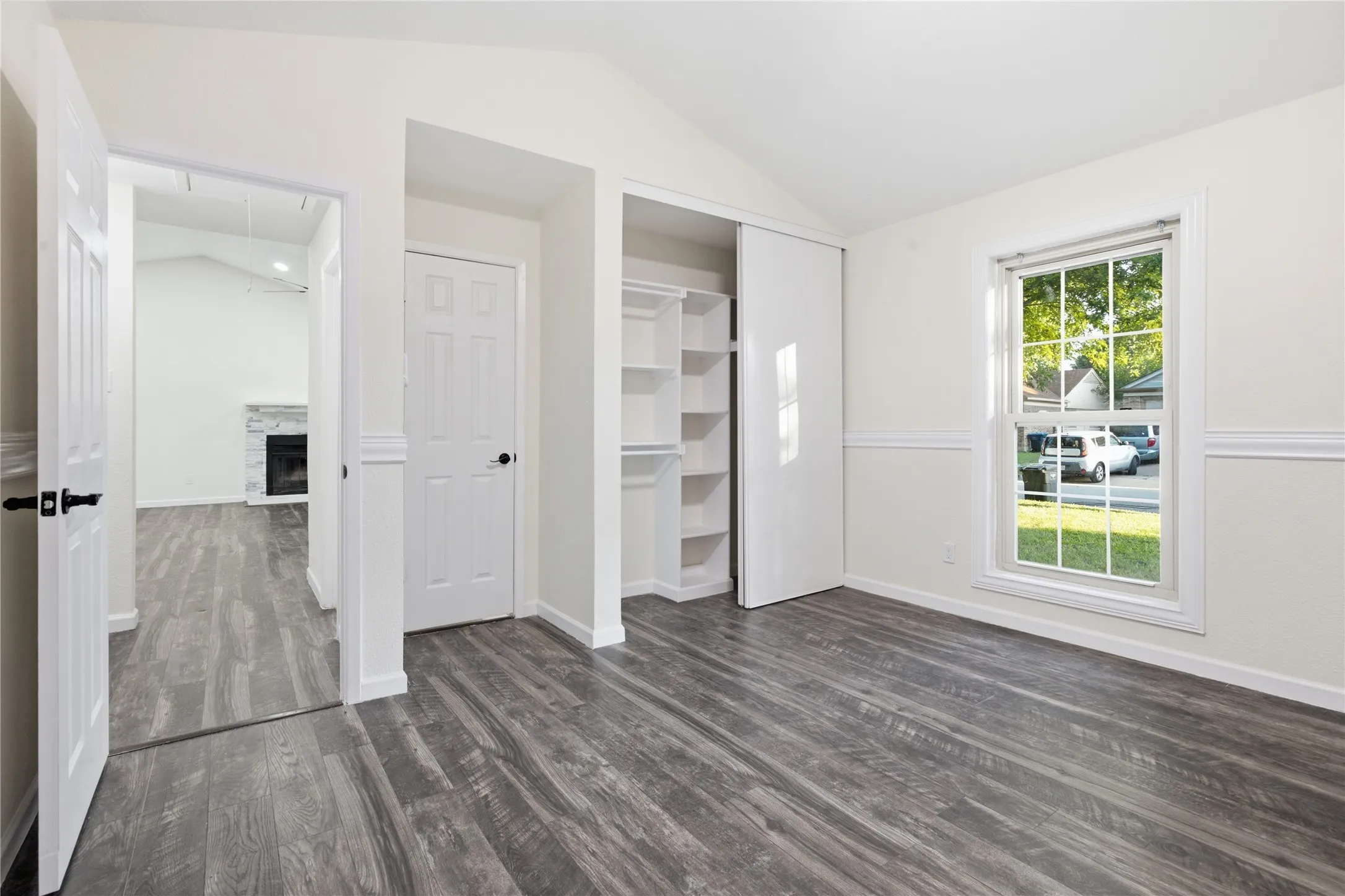Vaulted ceiling, wood-finish flooring, paneled interior doors, built-in closet shelving, and a large window