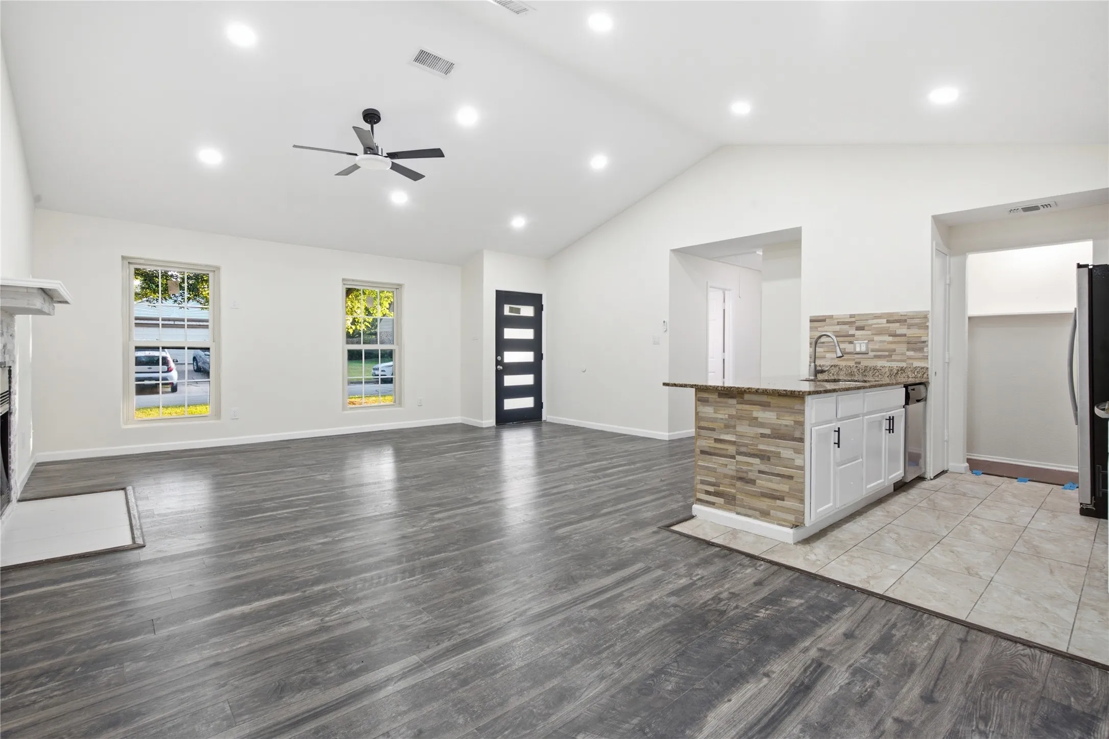 Vaulted ceilings, wood-finish flooring, recessed lighting, ceiling fan, and a kitchen island with a stone backsplash