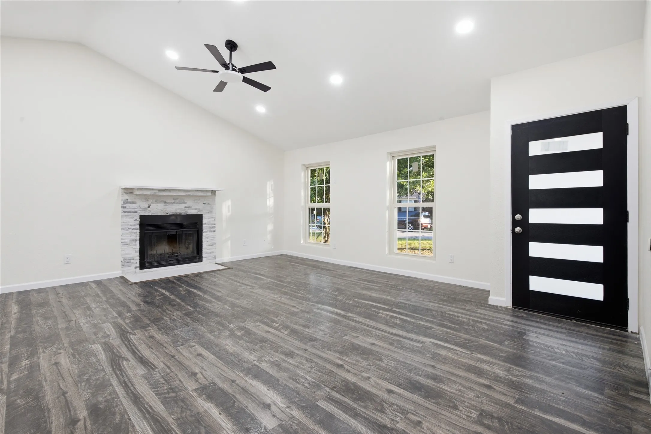 Vaulted ceiling, recessed lighting, ceiling fan, wood-finish flooring, and a fireplace with a stone surround