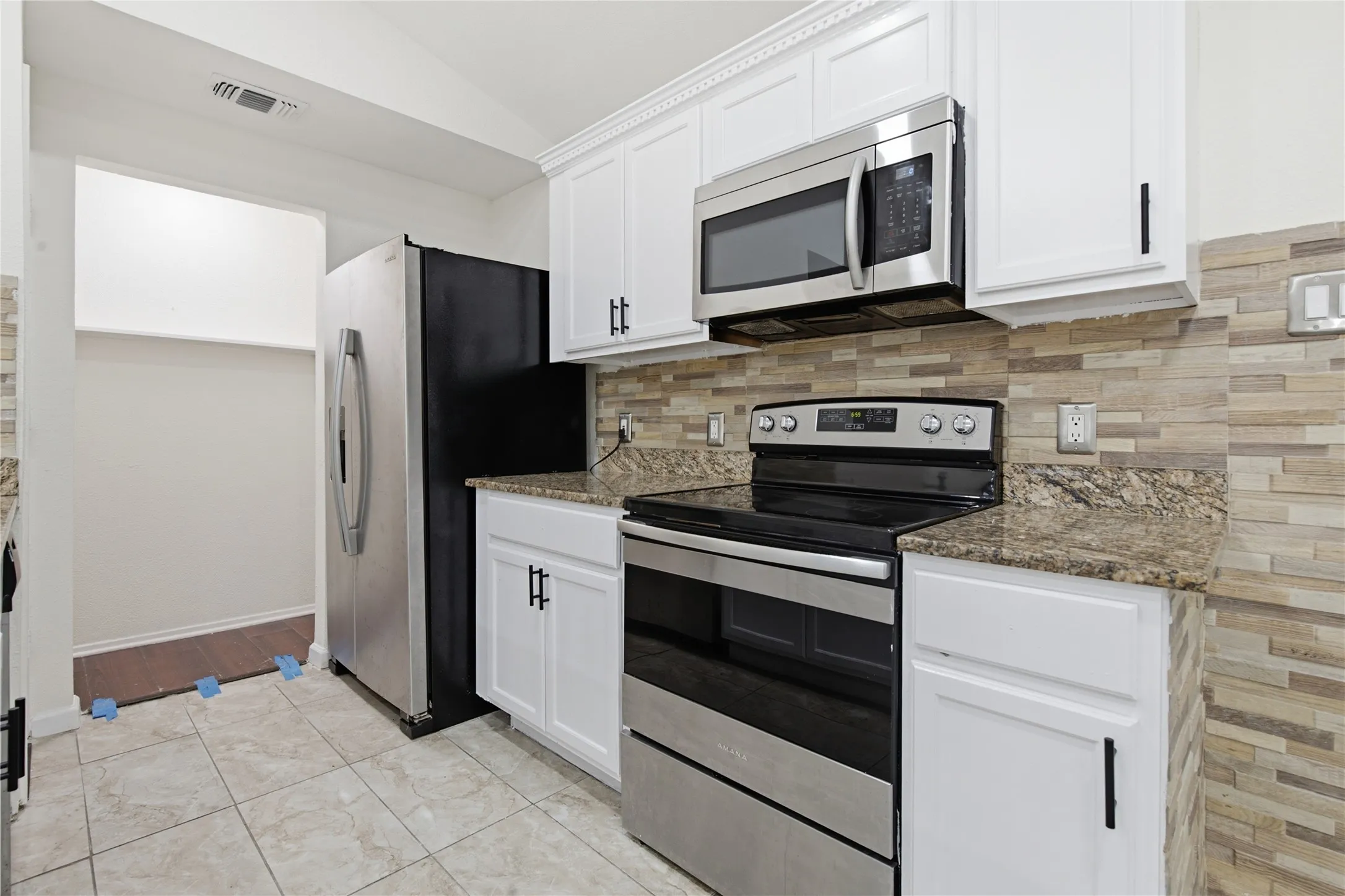White cabinetry, granite countertops, and a stacked stone backsplash