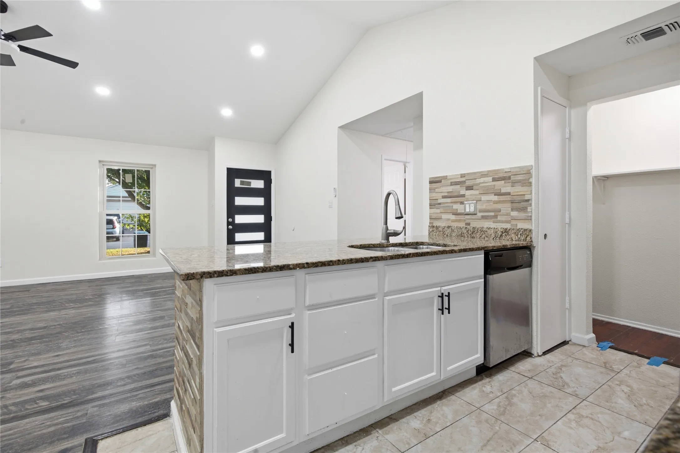 Kitchen island with stone-finish countertop, white cabinetry, and stainless steel dishwasher
