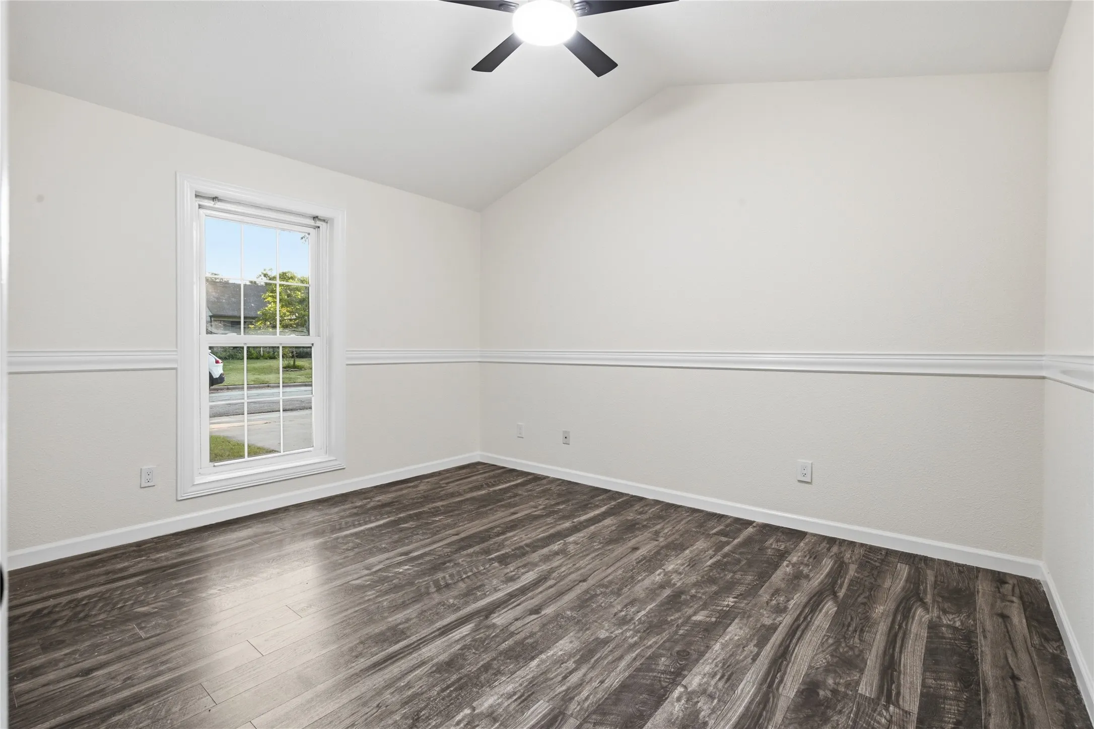 Vaulted ceiling with a ceiling fan, window with white trim, chair rail molding, and wood-finish flooring