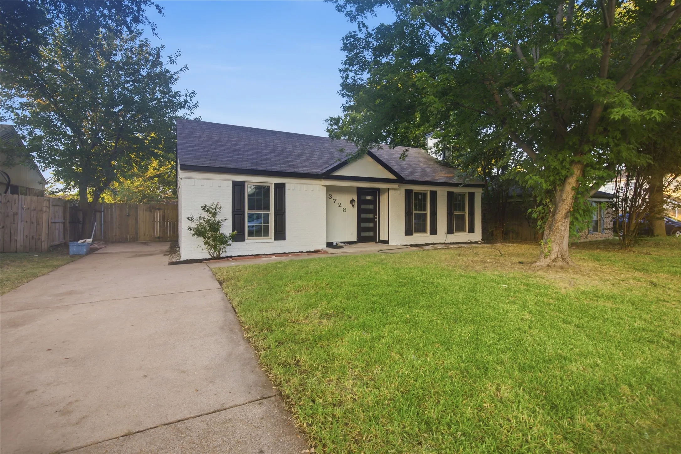 White brick exterior with black shutters, dark shingle roof, and a concrete driveway