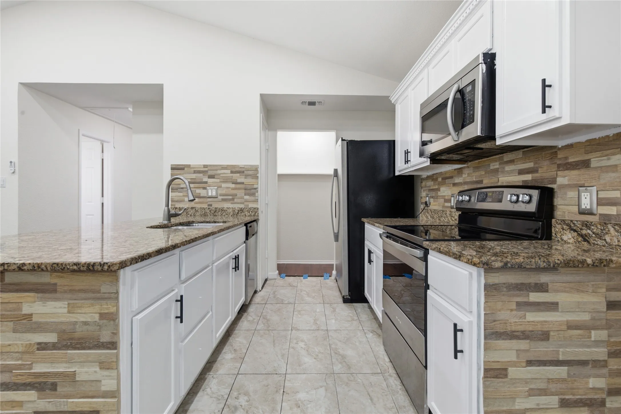 Kitchen featuring stone-look tile flooring, white cabinetry, granite countertops, and stainless steel appliances
