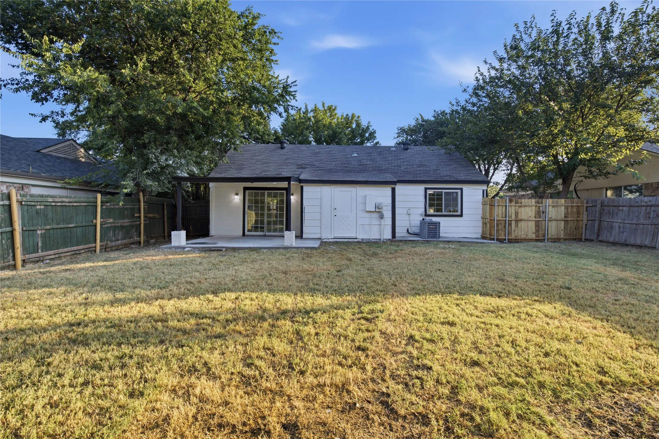 Rear exterior featuring a concrete patio, sliding glass doors, and a wood privacy fence