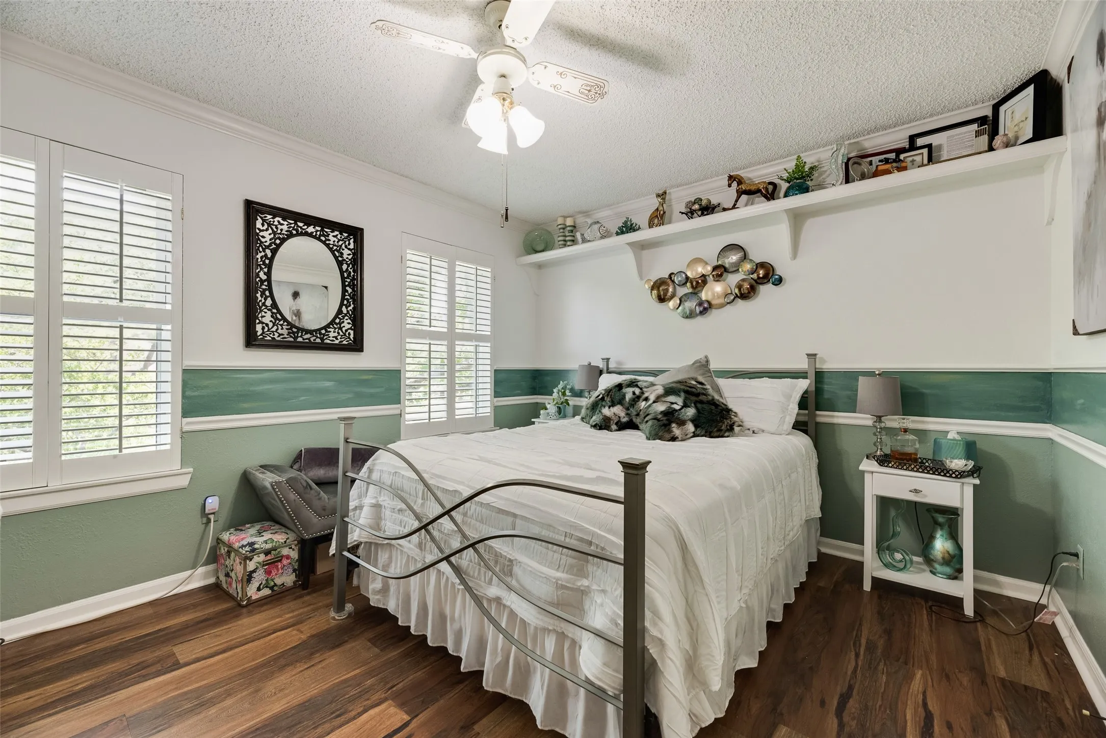 Wood-finish flooring, white plantation shutters, built-in shelving, white crown molding, and a ceiling fan with integrated lighting