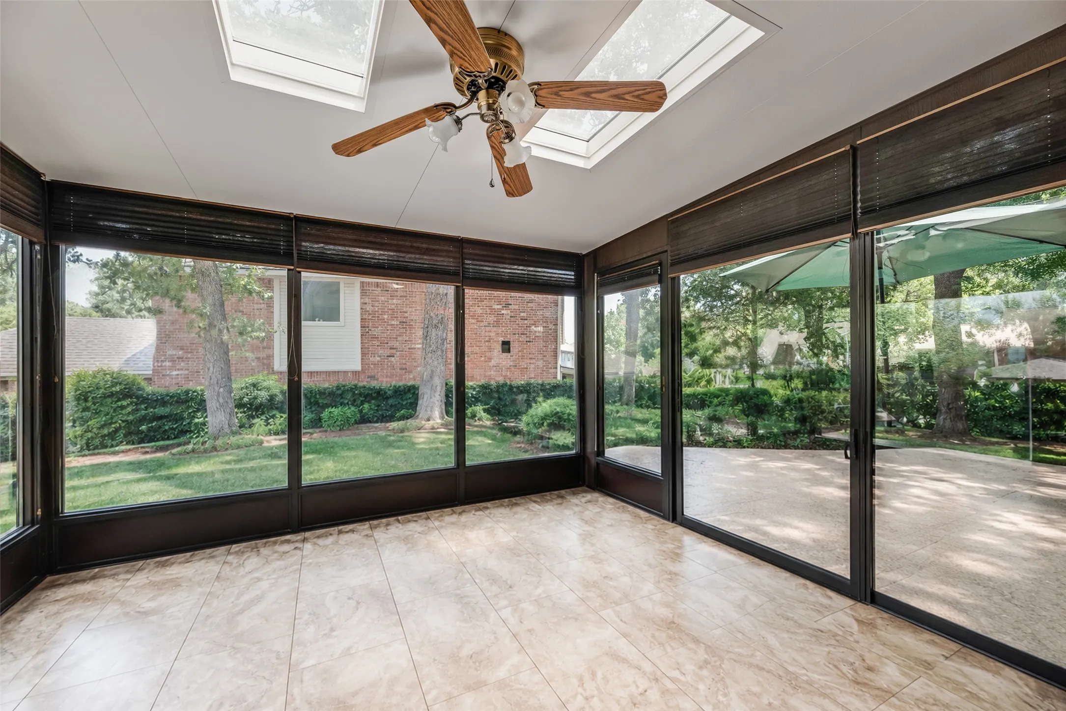 Enclosed sunroom featuring a ceiling fan, dual skylights, tile flooring, and extensive window panels