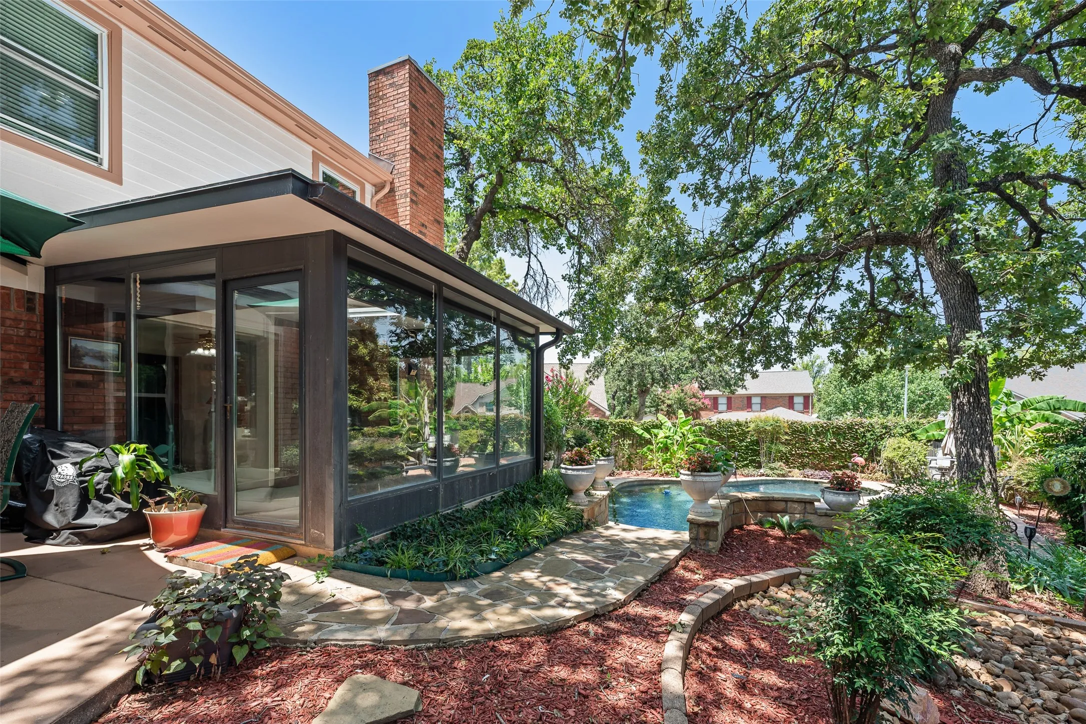 Sunroom with extensive glazing, flagstone patio, integrated spa, and mature trees