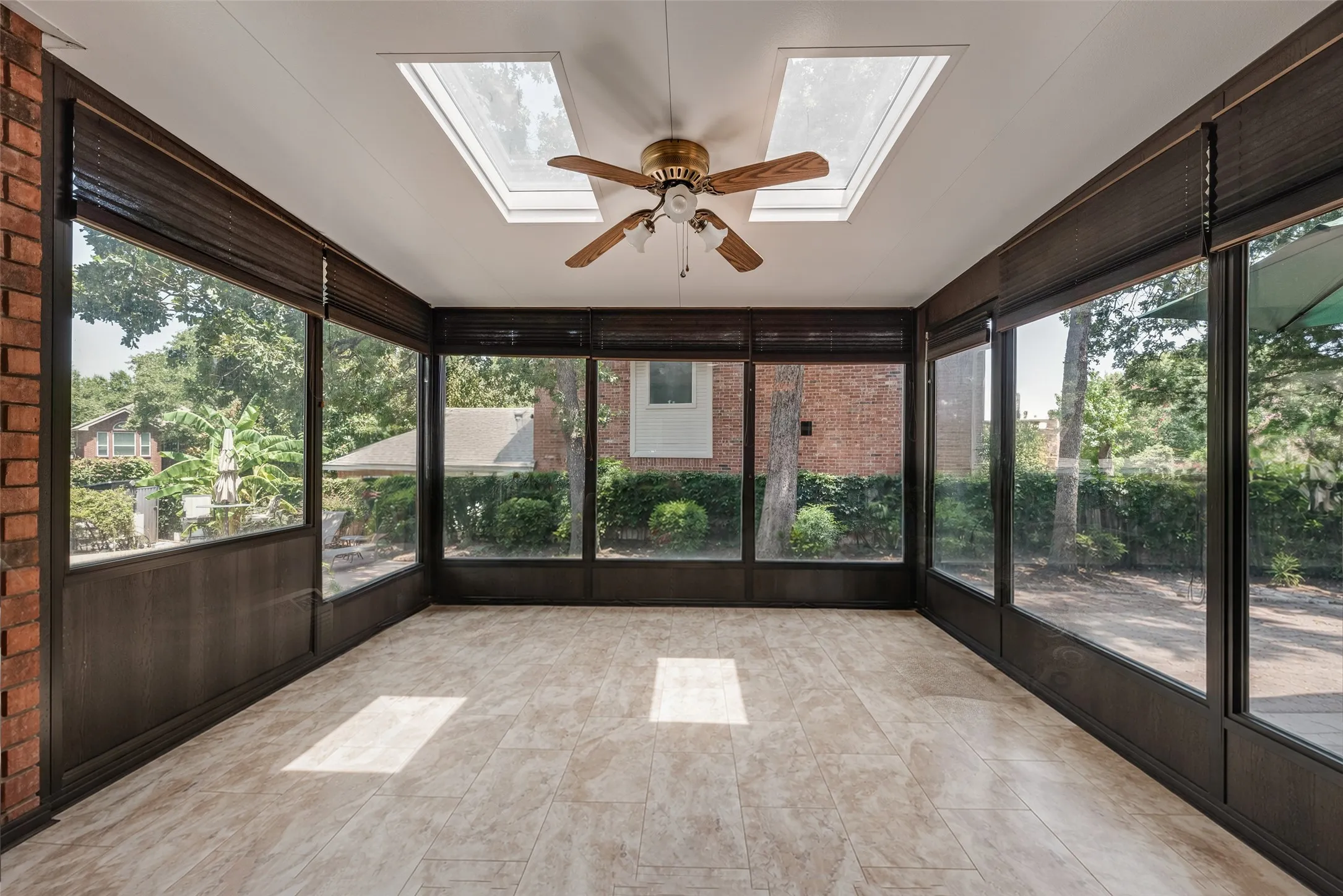 Sunroom featuring expansive windows, two skylights, a ceiling fan, and light-toned tile flooring