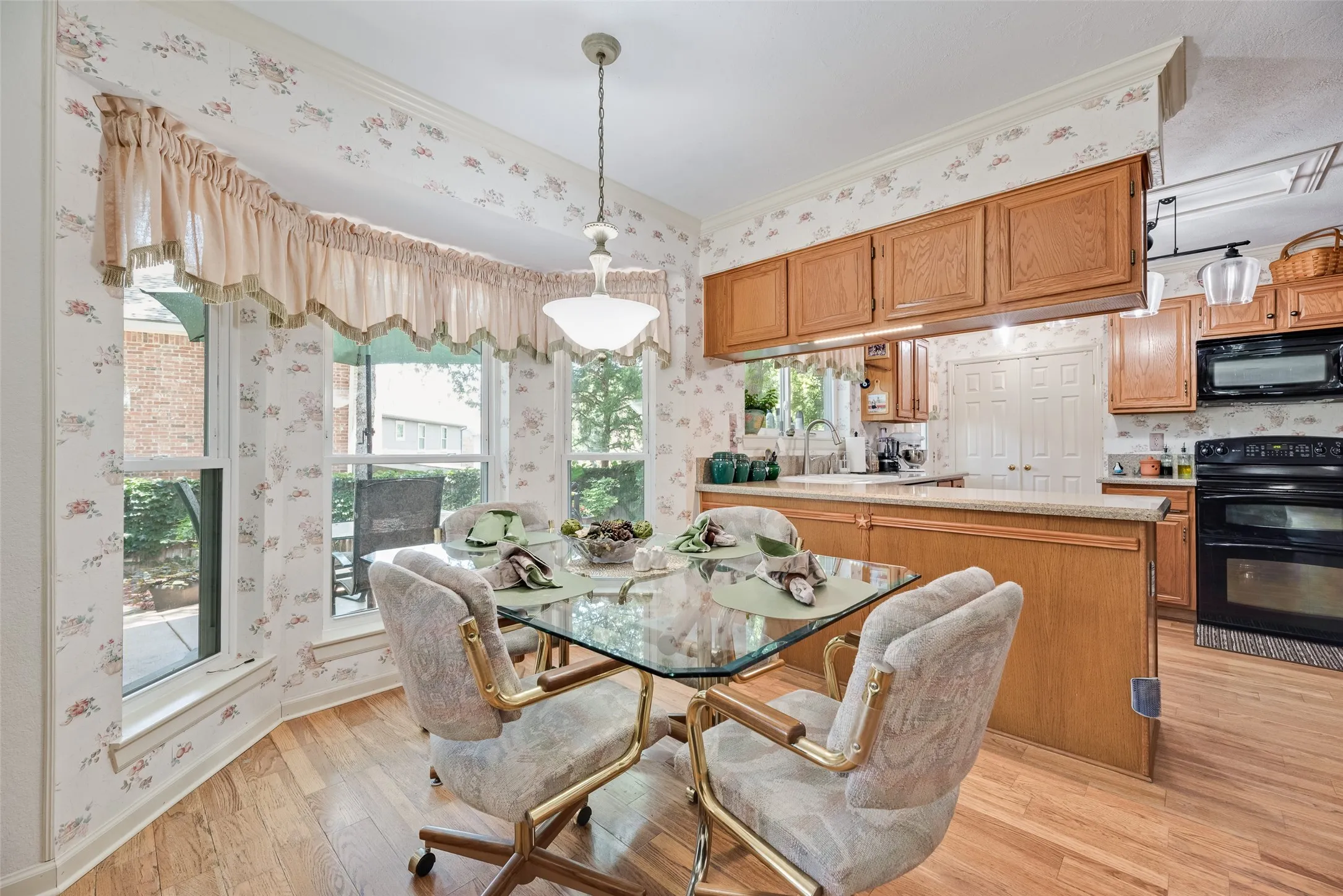 Bay window with valance, wood-finish flooring, recessed lighting, wood cabinetry, and black appliances
