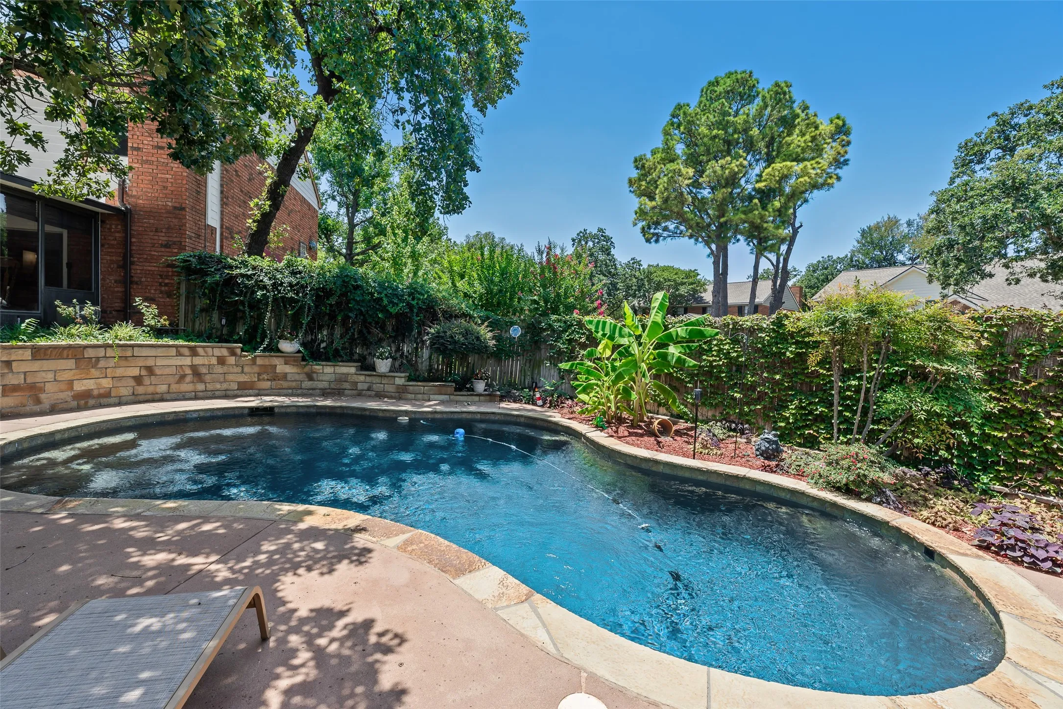 Private backyard oasis featuring a curved swimming pool, stone coping, and a surrounding concrete patio
