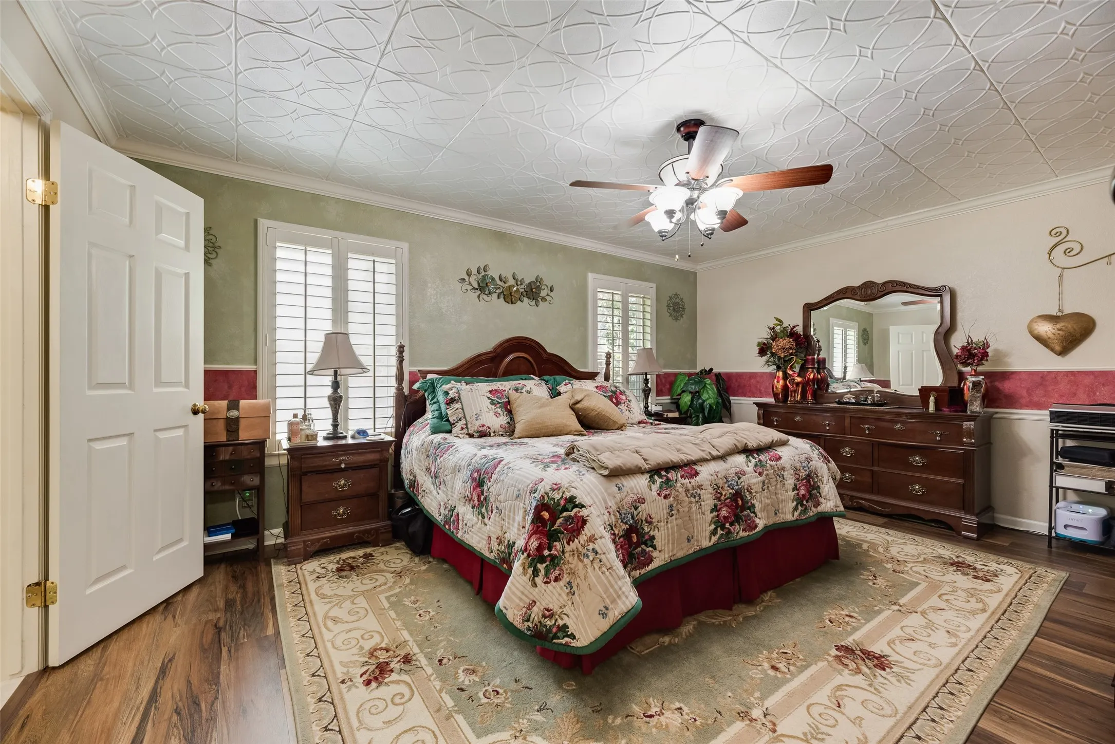 Tray ceiling with decorative molding, wood-finish flooring, white plantation shutters, and a ceiling fan with light fixture