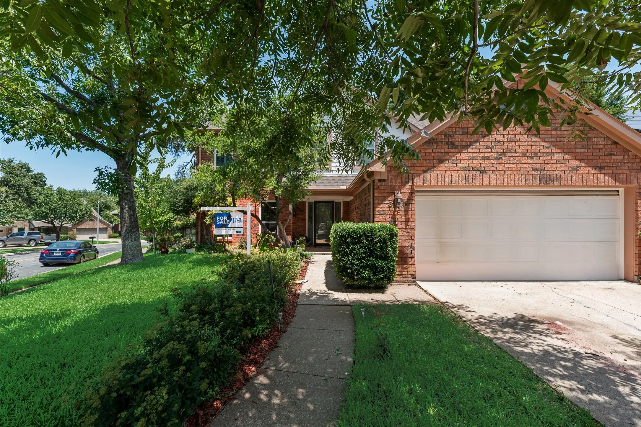 Brick exterior with an attached garage, concrete driveway, and mature landscaping