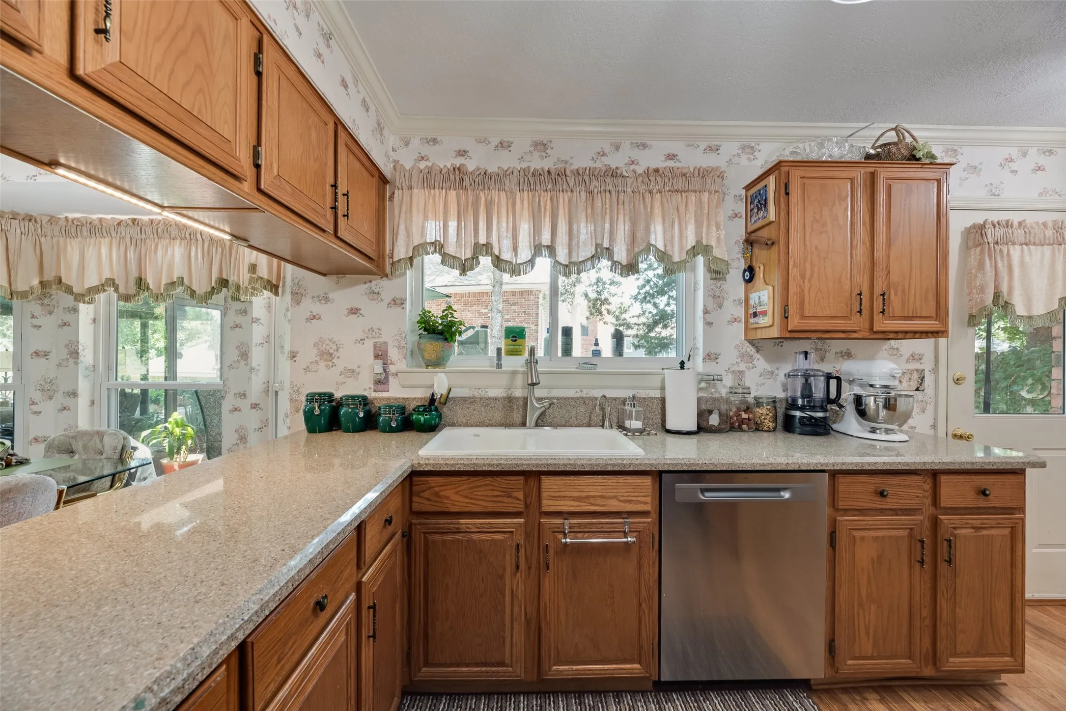 Kitchen featuring wood cabinetry, light-toned countertops, a stainless steel dishwasher, and a white basin sink