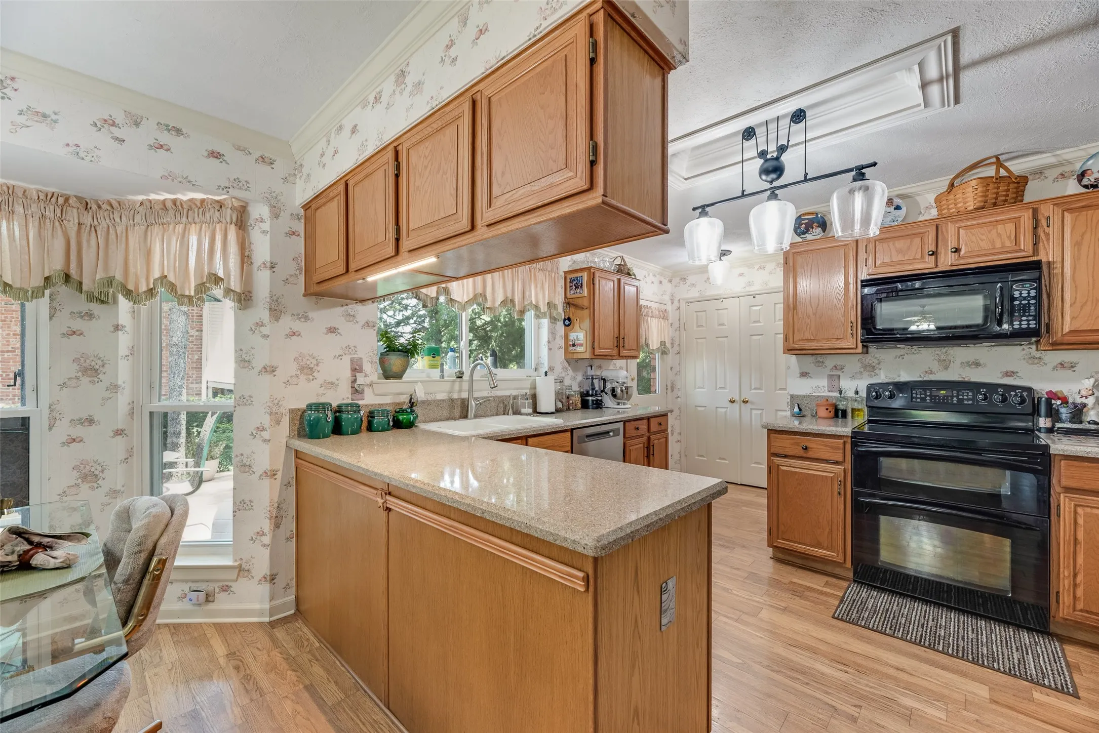 Kitchen featuring wood-finish flooring, overhead lighting, wood cabinetry, stone countertops, and a double-oven range