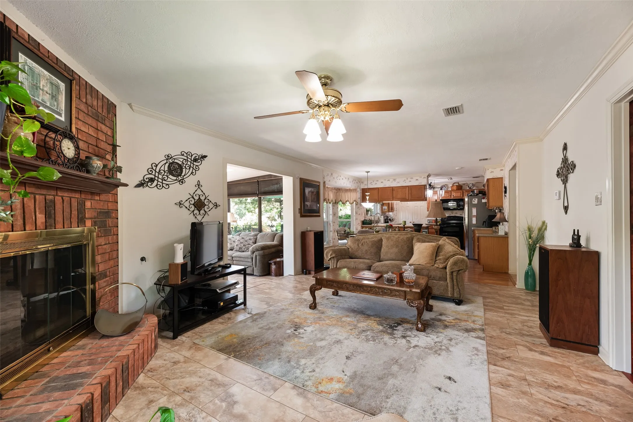 Brick-faced fireplace with a wood mantel, tile flooring, and a ceiling fan with integrated lighting