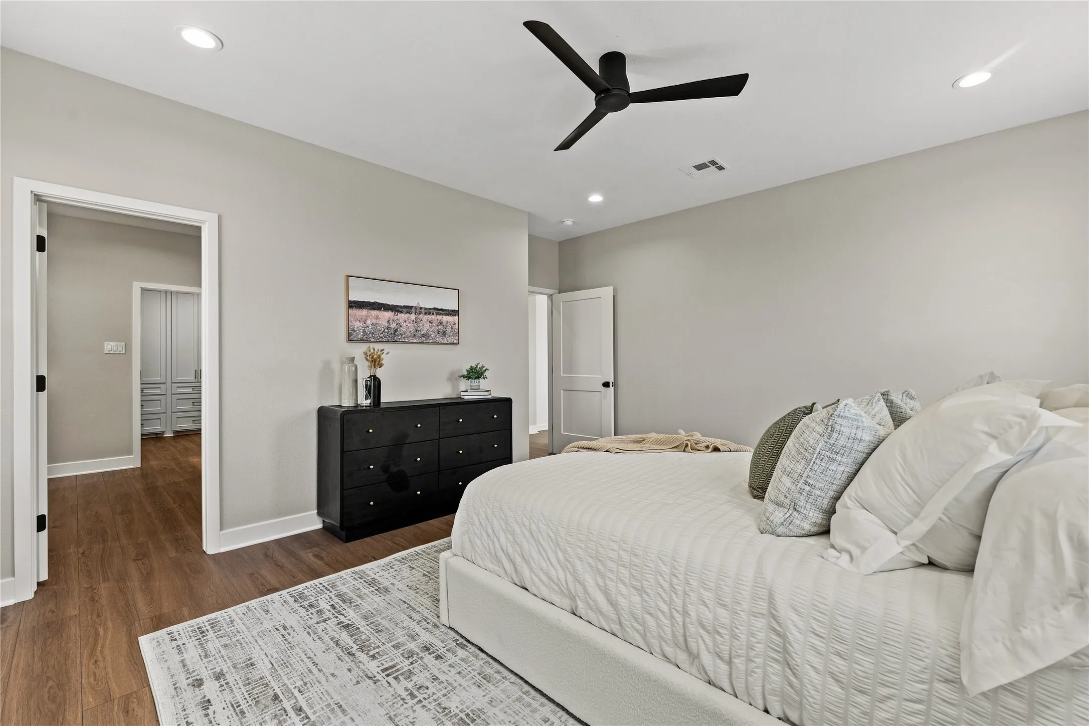 Wood-finish flooring, recessed lighting, and a modern ceiling fan complement the light-toned walls
