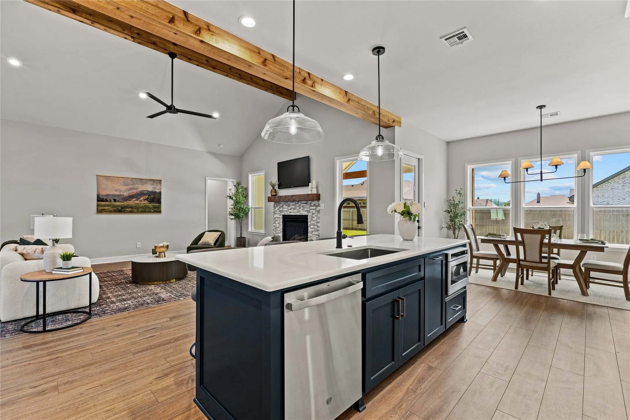 Vaulted ceilings with exposed wood beams, wood-finish flooring, central kitchen island with integrated sink, stainless steel appliances, and a dining area with multiple windows