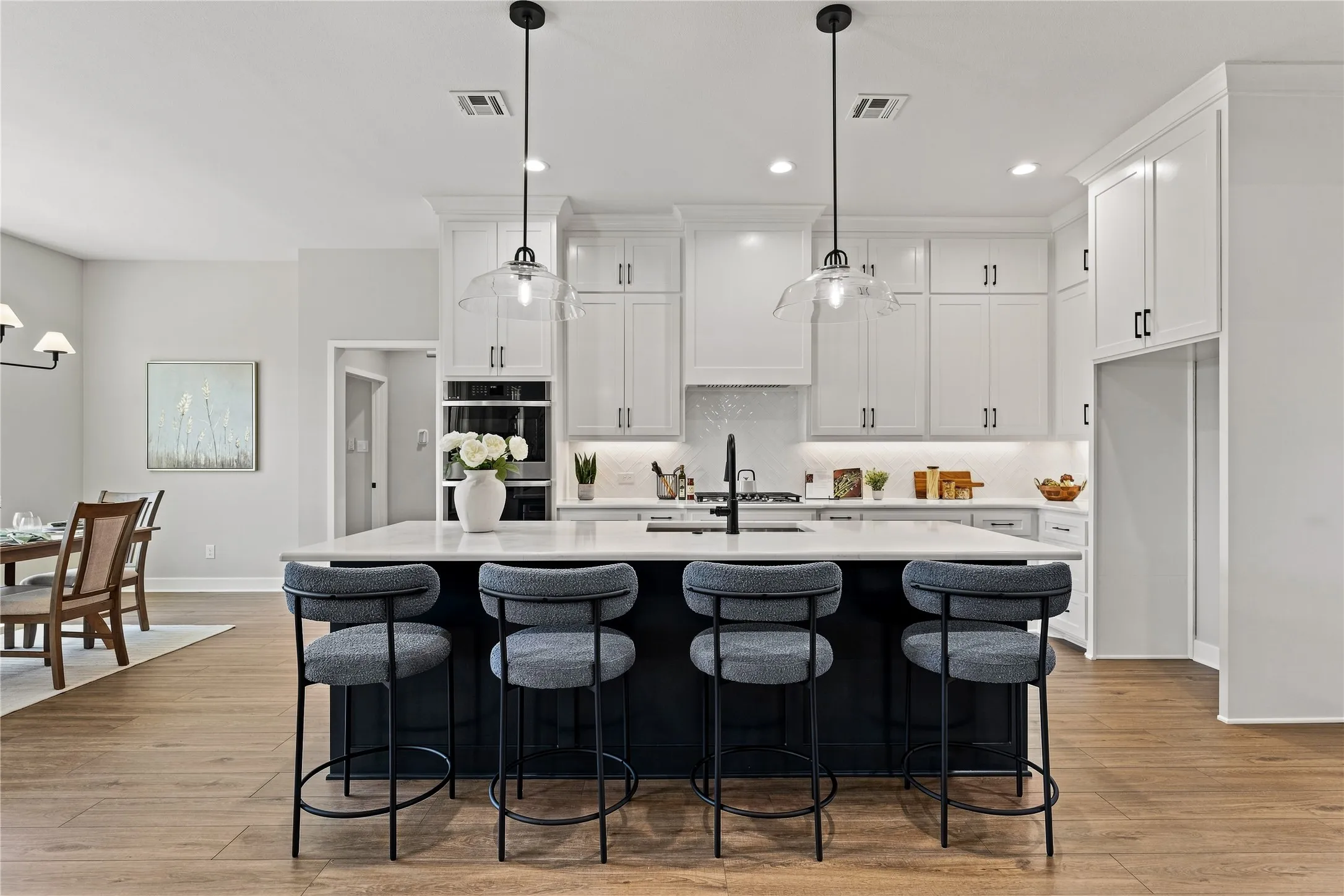 Bright kitchen with white cabinetry and a contrasting center island, integrated wall oven, and wood-finish flooring
