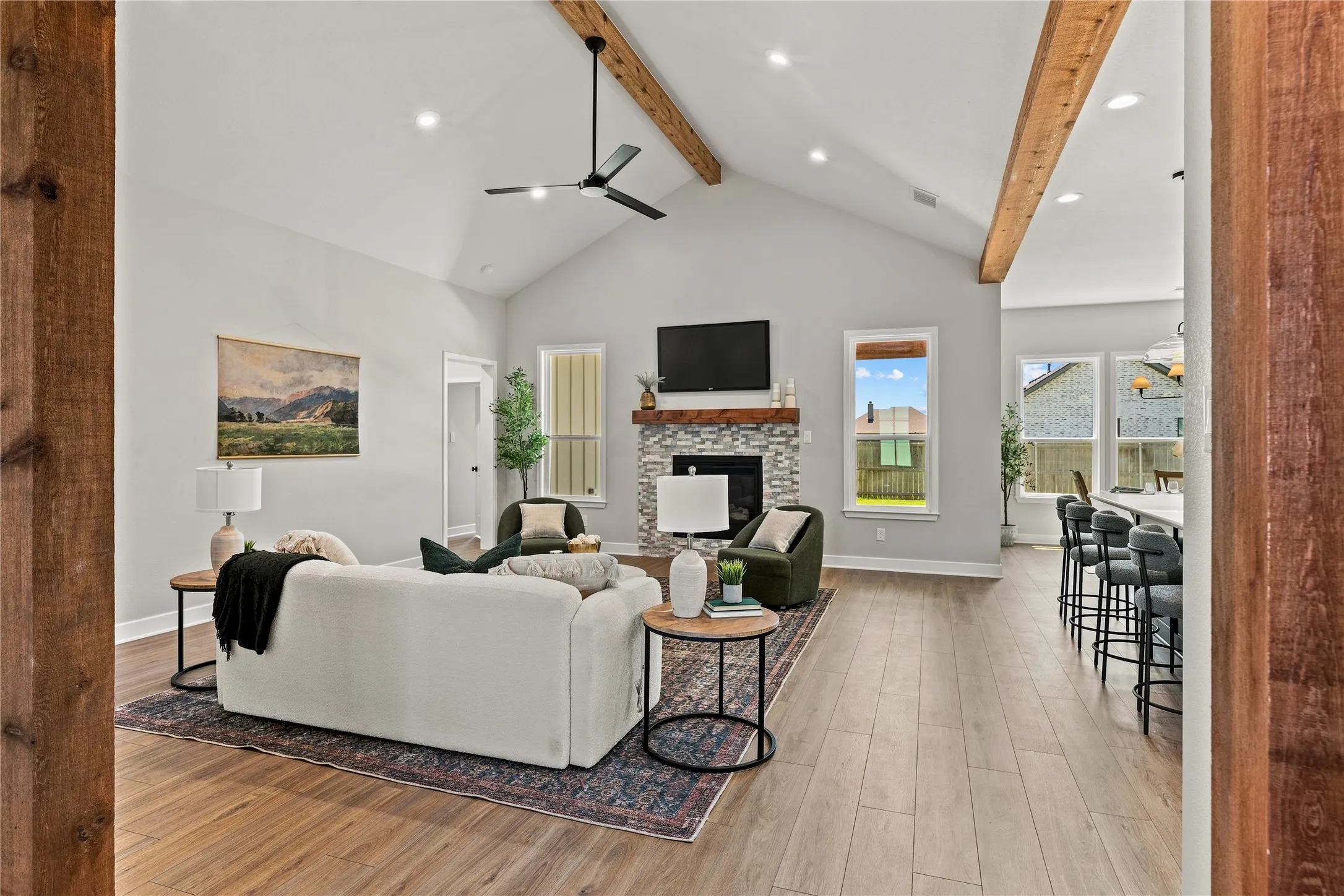 Vaulted ceiling with exposed wood beams, wood-finish flooring, stone-clad fireplace with wood mantle, recessed lighting, and a contemporary ceiling fan
