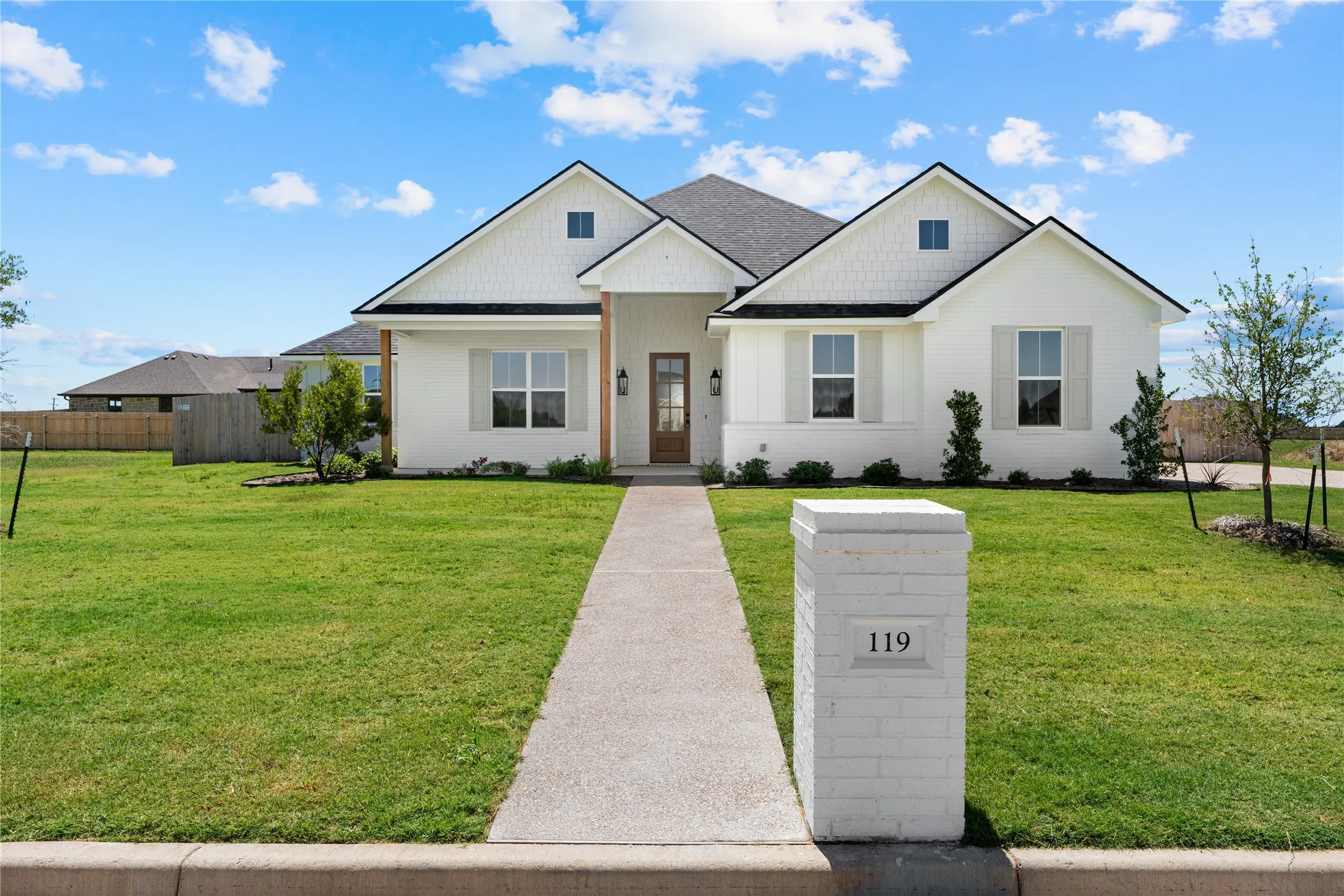 Exterior featuring white painted brick, dark shingle roof, wood-finish columns, and a concrete walk-up