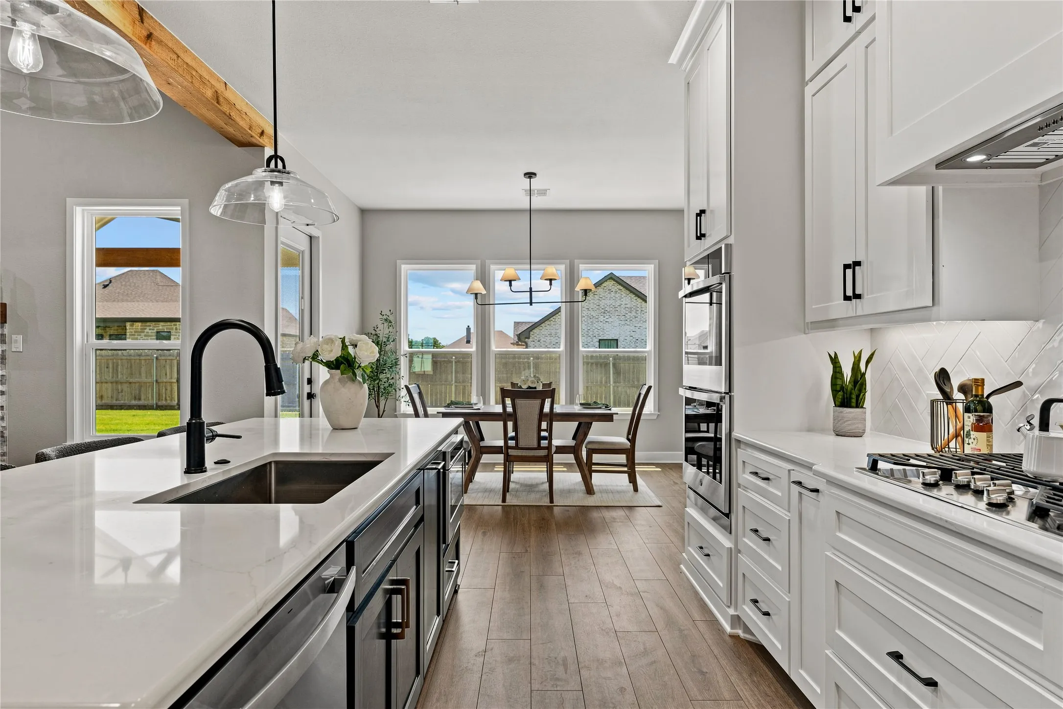 Modern kitchen featuring wood-finish flooring, white cabinetry, integrated stainless steel appliances, a center island with sink, and clear glass pendant lighting