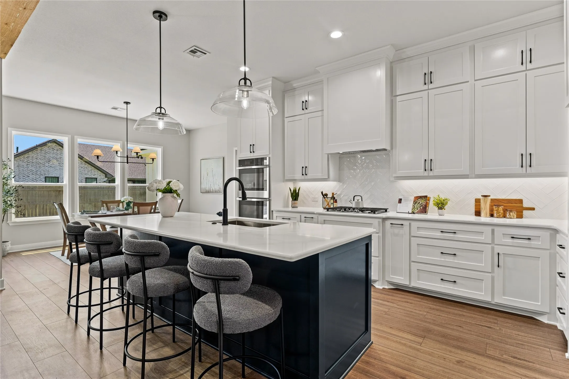 Gourmet kitchen with a large central island, white shaker cabinetry, stainless steel appliances, and wood-finish flooring