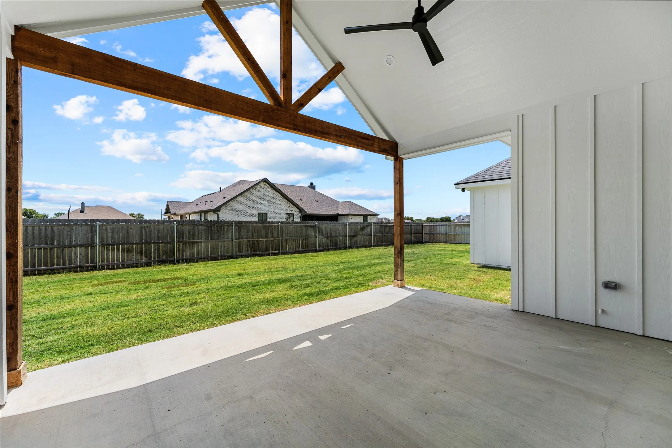 Covered outdoor patio featuring exposed wood beams, a vaulted ceiling, and a modern ceiling fan