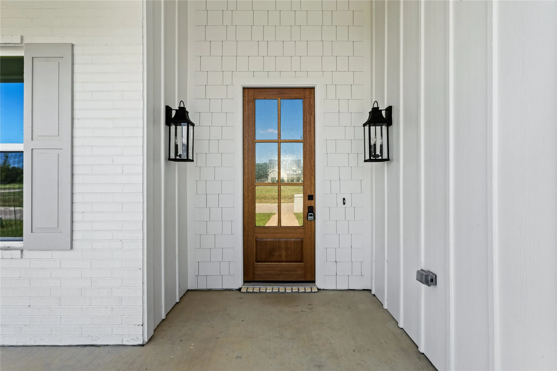 Wood-finish front door with clear glass panels, flanked by two black lantern-style sconces