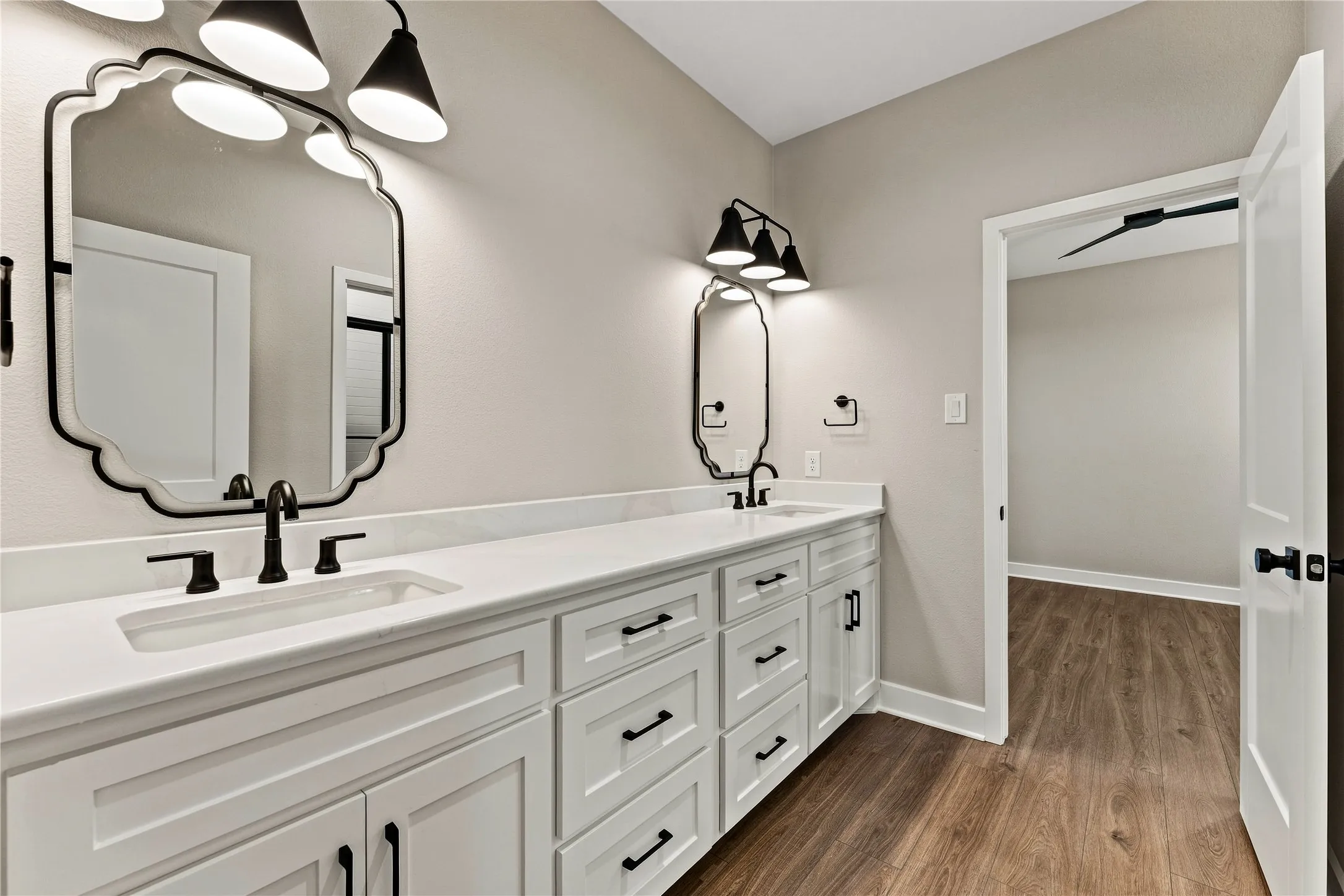 Dual vanity with white cabinetry and dark hardware, integrated sinks, white countertops, and wood-finish flooring