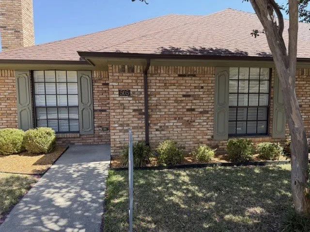 Brick exterior with a brown shingle roof, green window shutters, and a concrete pathway