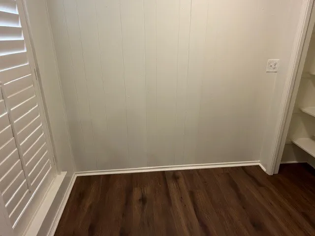 White wainscoting with wood-finish flooring, plantation shutters, and built-in shelving
