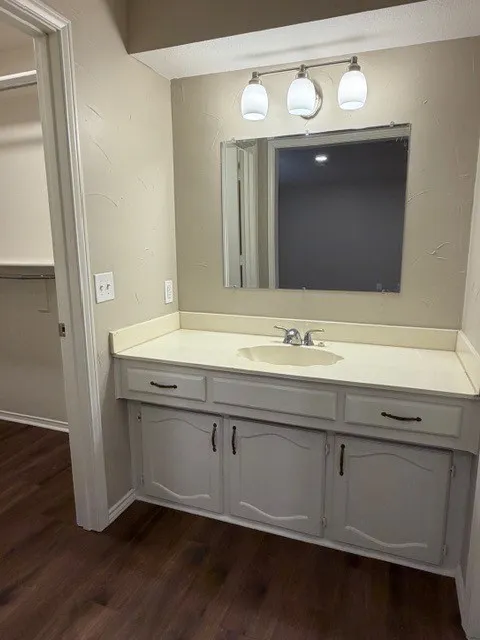 Vanity with a single basin sink, white cabinetry, integrated countertop, and a wall-mounted light fixture