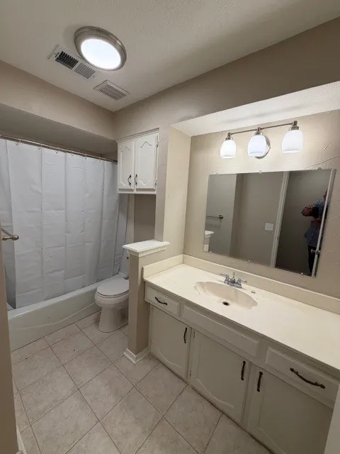 Tiled flooring, vanity with integrated sink, overhead vanity lighting, built-in storage cabinetry, and a tub/shower combination