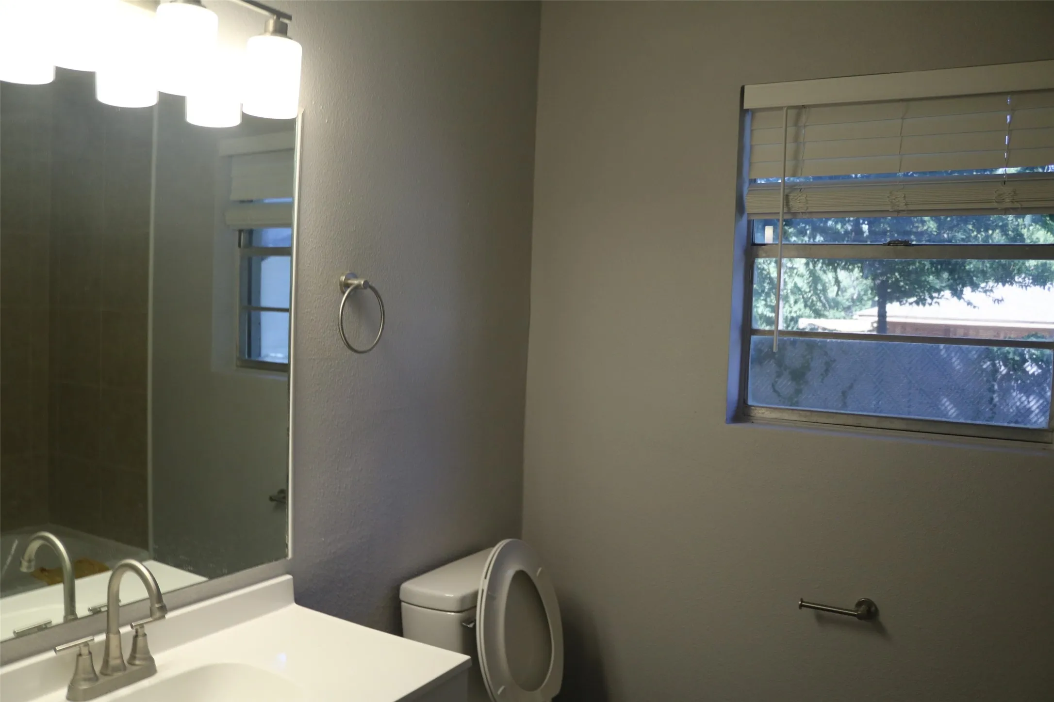 Bathroom featuring a vanity with a rectangular sink, a wall-mounted mirror, overhead light fixture, and a window with blinds